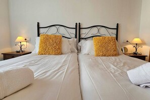 Un lit double avec du linge de lit blanc et deux coussins décoratifs, de part et d’autre duquel se trouvent des tables de chevet avec des lampes.