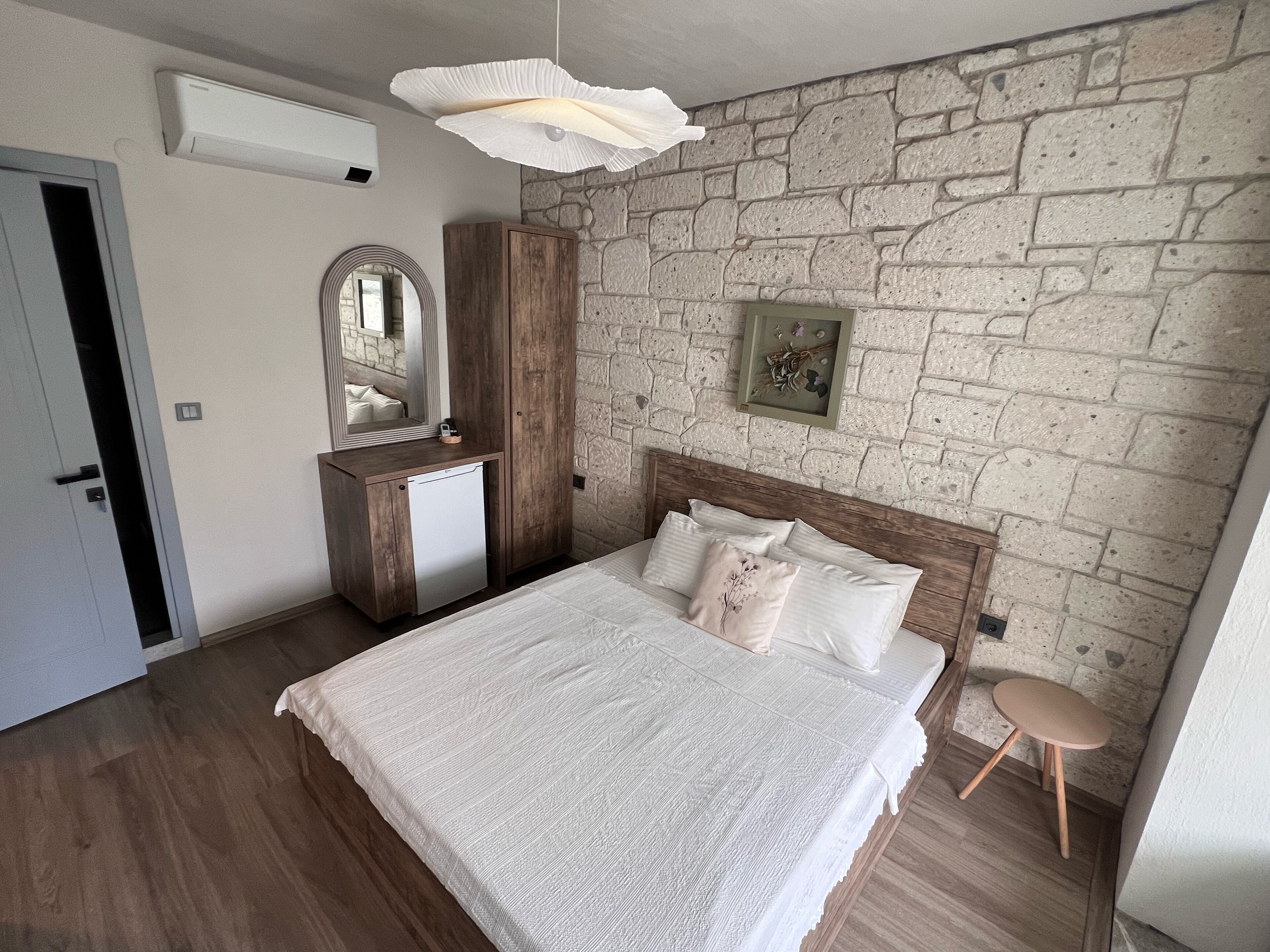 A bedroom with a stone wall, a wooden wardrobe, a bedside table, and a bed with white bedding.