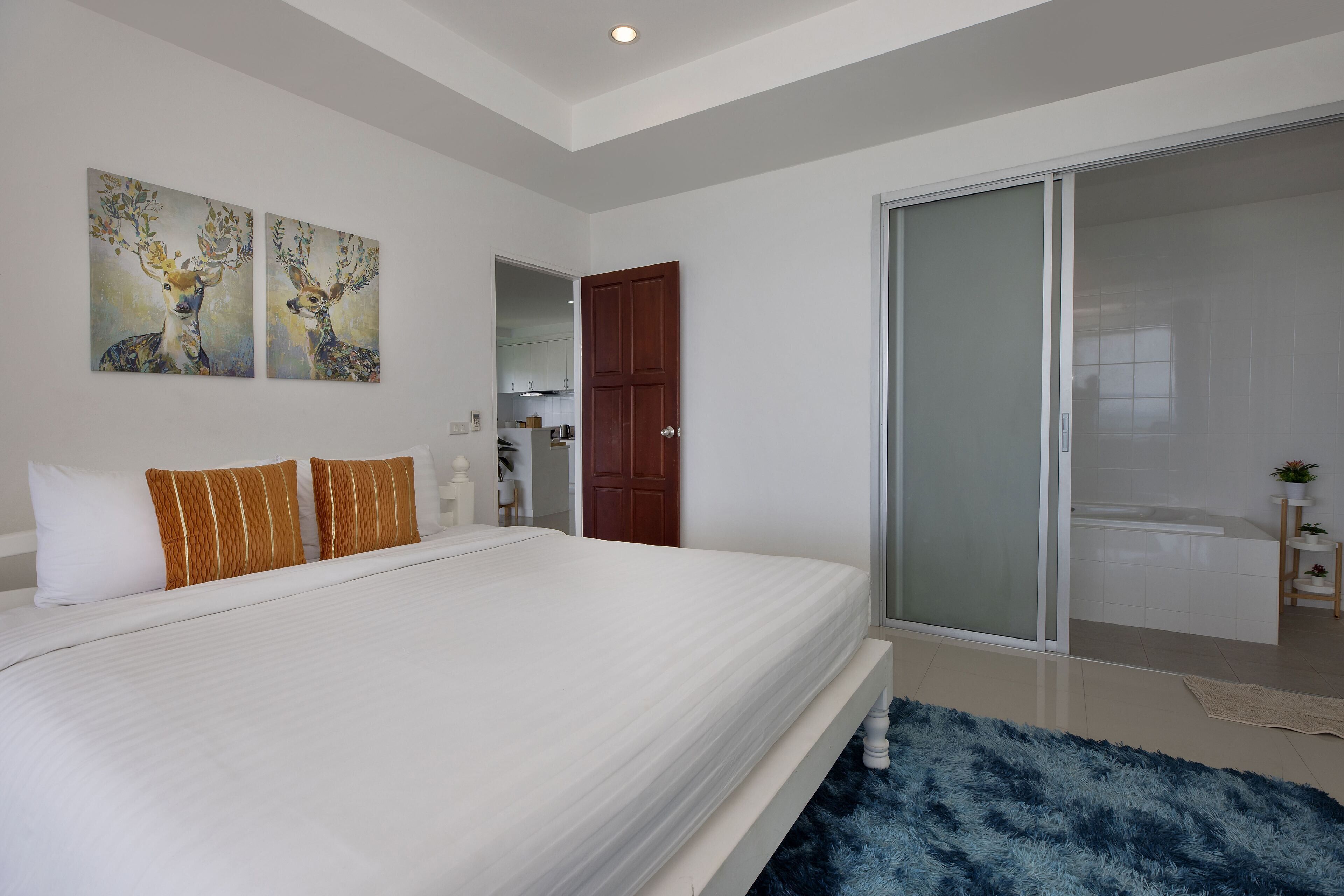 Une chambre moderne avec un grand lit, une porte-fenêtre coulissante donnant sur une salle de bain et deux tableaux accrochés au mur.