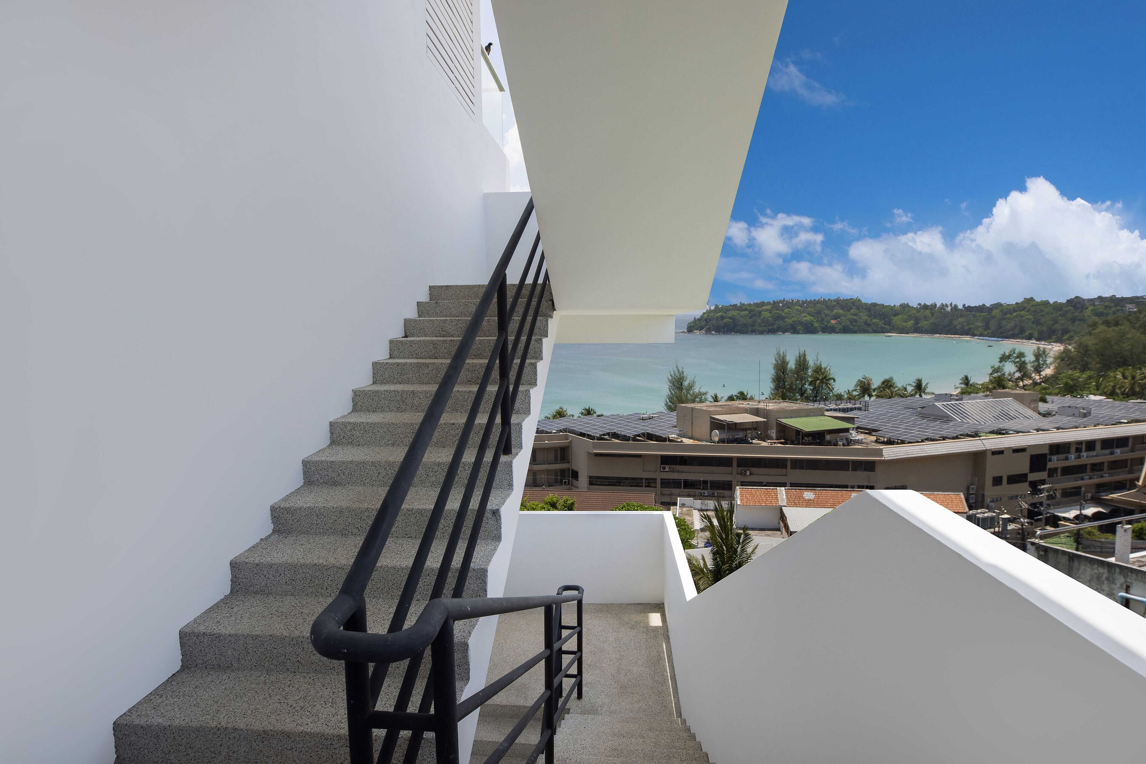 A staircase leading to a balcony overlooking a coastal area with buildings and a clear sky.