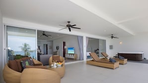 A spacious living area with large wicker sofas, a flat-screen TV, ceiling fans, and a hot tub. - Ocean View Jacuzzi 3BR Kata Penthouse (Karon)