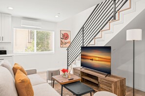 A modern living room with a flat-screen TV, a staircase, and a view of the outdoors through large windows. - Modern Home Near Pasadena Garage Full Kitchen (Alhambra)
