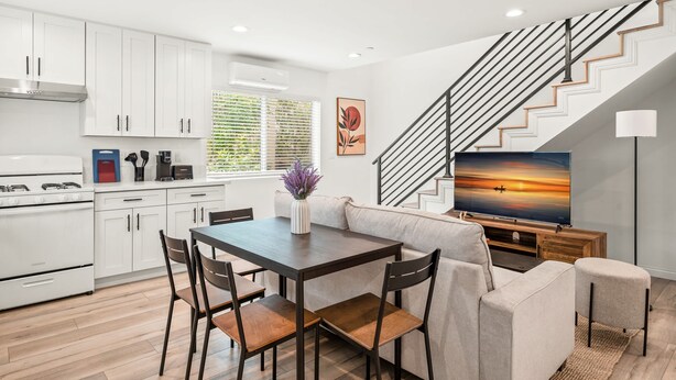 A modern kitchen with white cabinets, a dining table with chairs, a sofa, a TV, and a staircase. - Modern Home Near Pasadena Garage Full Kitchen (Alhambra)