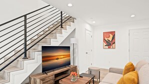 A modern living room with a staircase, a flat-screen TV, a coffee table with flowers, and a sofa with yellow cushions. - Modern Home Near Pasadena Garage Full Kitchen (Alhambra)