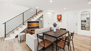 A modern living room with a dining area, a staircase, and a kitchen visible through an archway. - Modern Home Near Pasadena Garage Full Kitchen (Alhambra)