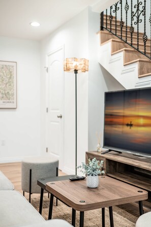 Un salon moderne avec une table basse en bois, un lampadaire, un téléviseur et un escalier doté d’une rampe.