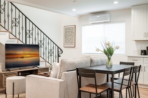 Un salon moderne doté d’un téléviseur à écran plat, d’un canapé, d’une table à manger avec des chaises, d’un escalier avec des rampes décoratives et d’une fenêtre avec des stores.