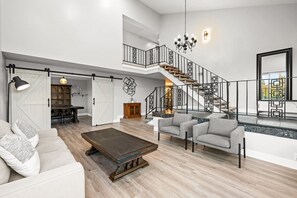 A spacious living area with a high ceiling, a staircase with geometric railing, and a dining area in the background. - Luxury Hilltop Stay Pool Views Sleeps Many (Hacienda Heights)