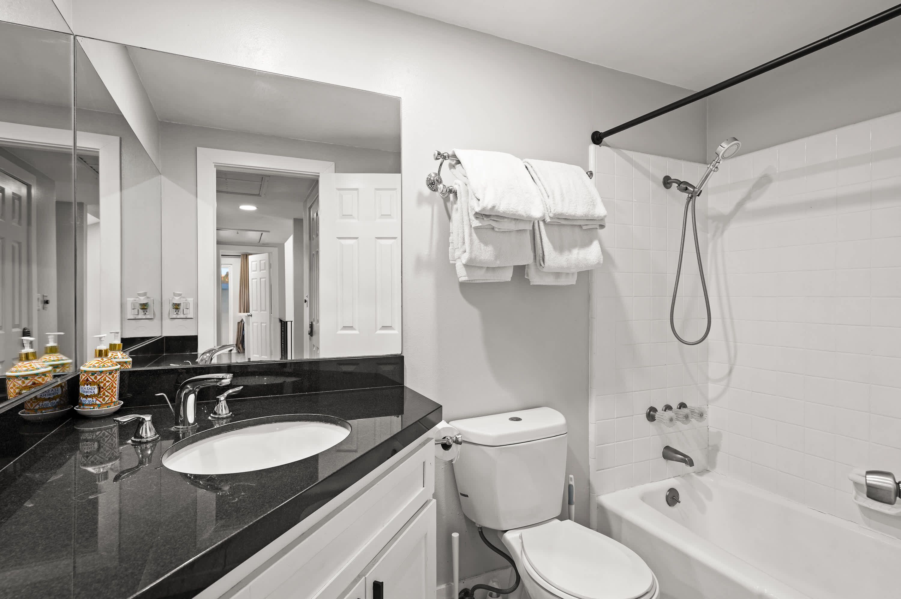 A modern bathroom with a black countertop sink, white toilet, and bathtub.