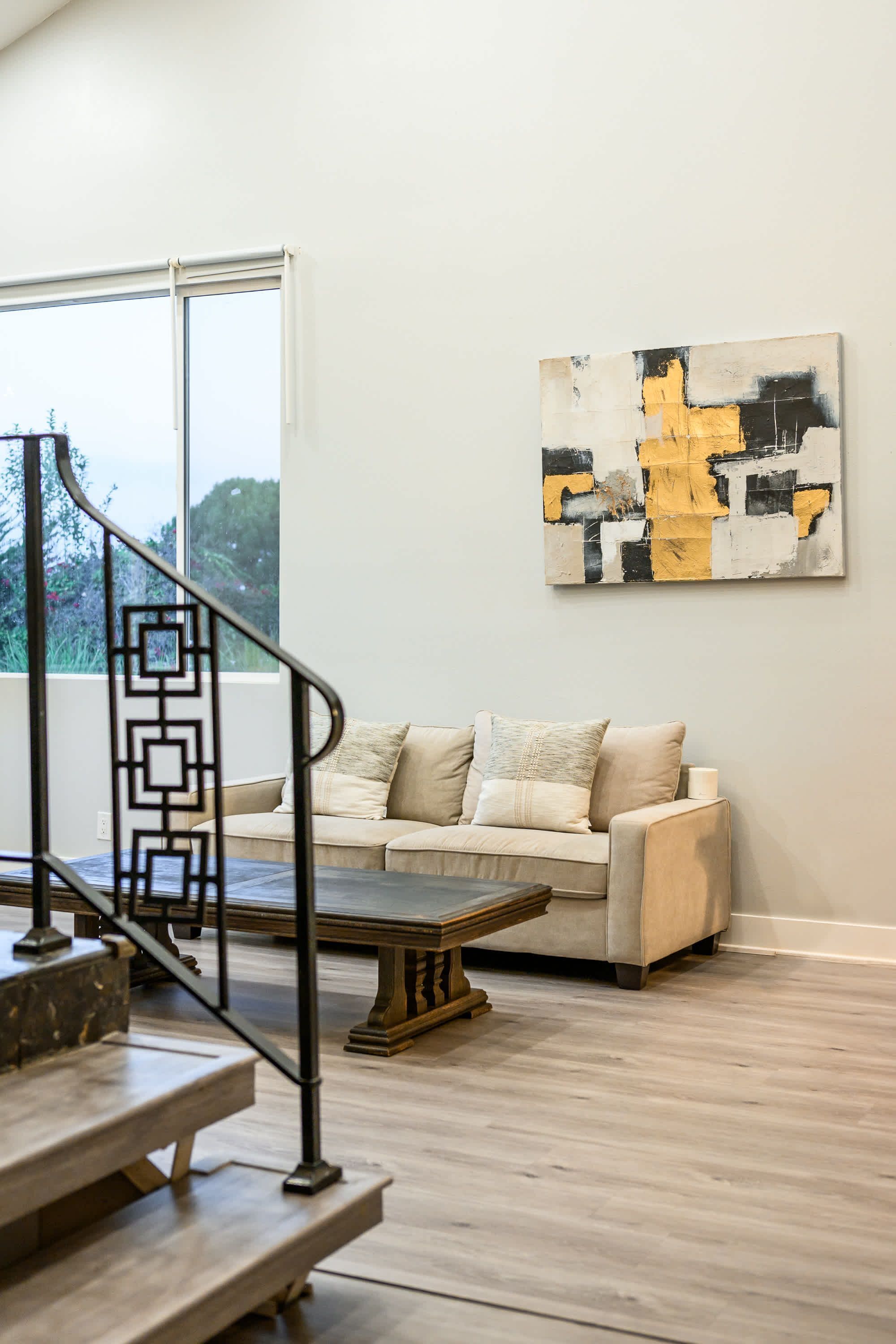 Un salon moderne avec un escalier, un canapé beige et un tableau abstrait contemporain.