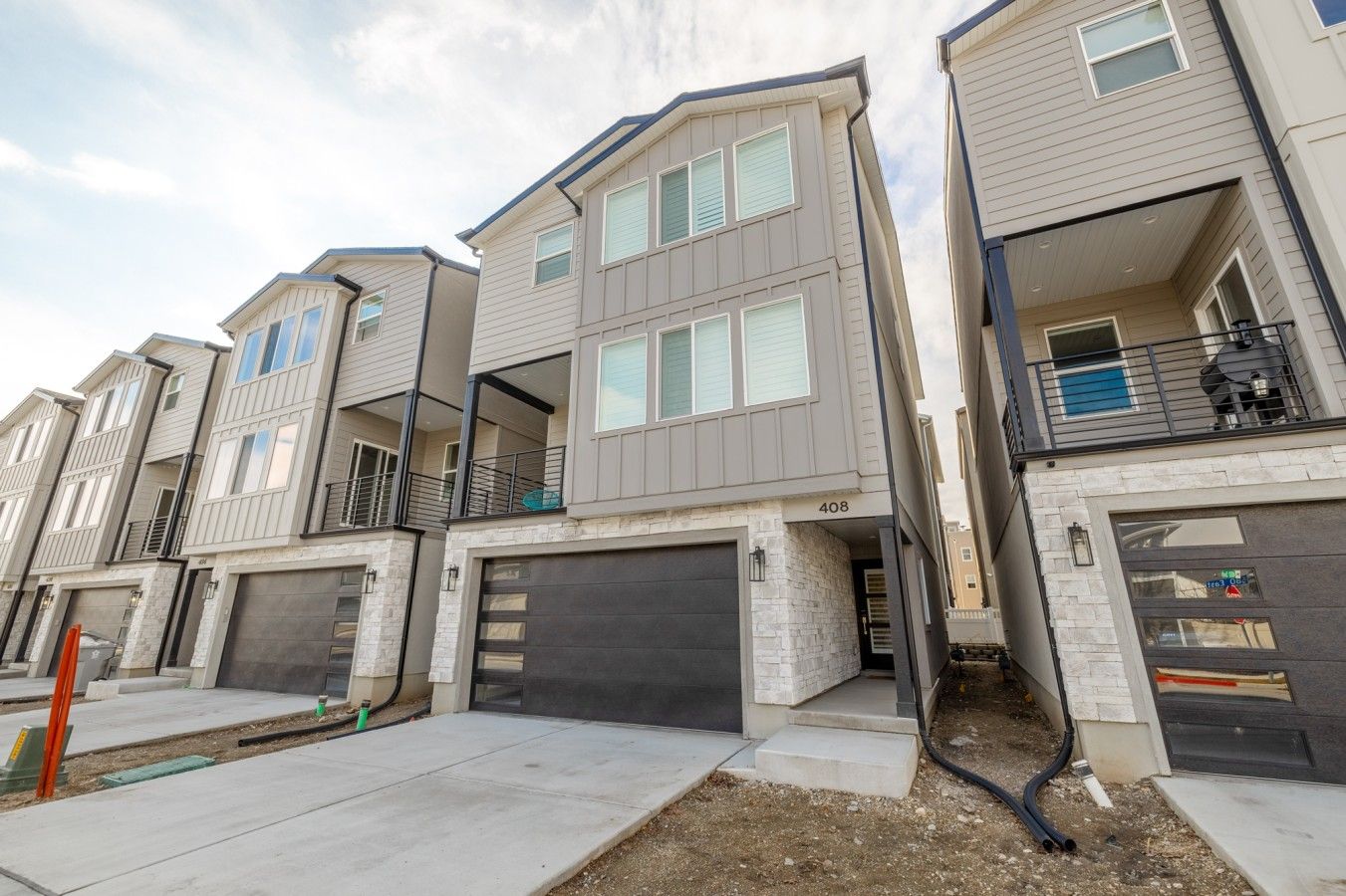A row of modern townhouses with attached garages, a stone facade, and a clear sky.