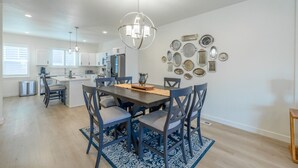 A modern kitchen with white cabinets, a dining area with a dark wooden table and blue chairs, and a decorative wall with metal plates. - Near American Fork Canyon | Family & Pet Friendly (American Fork)