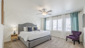 A bedroom with a bed, a chair, a nightstand, a ceiling fan, and a window with curtains. - Near American Fork Canyon | Family & Pet Friendly (American Fork)