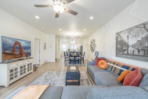 A spacious living room with a large flat-screen TV, a ceiling fan, and a dining area with a table and chairs. - Near American Fork Canyon | Family & Pet Friendly (American Fork)