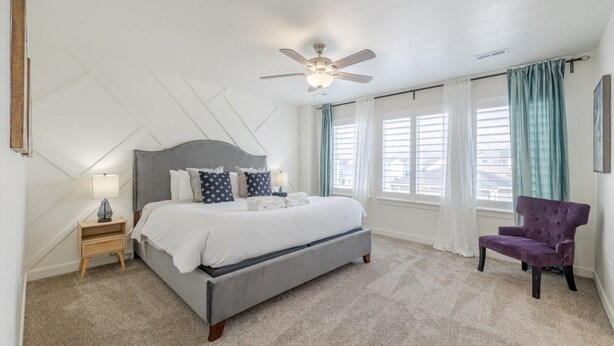 A bedroom with a bed, a chair, a nightstand, a ceiling fan, and a window with curtains. - Near American Fork Canyon | Family & Pet Friendly (American Fork)