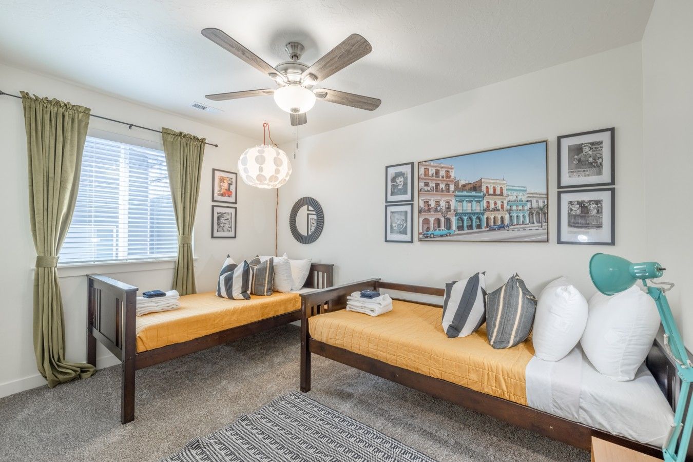 A room with two beds, a ceiling fan, a window with curtains, and wall art.