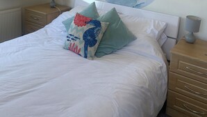 Une chambre à coucher avec un lit, deux tables de chevet, un tableau au mur et une fenêtre avec des rideaux.