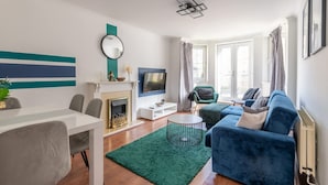 Ein modernes Wohnzimmer mit Kamin, einem blauen Sofa, einem Esstisch und einem Fernseher.