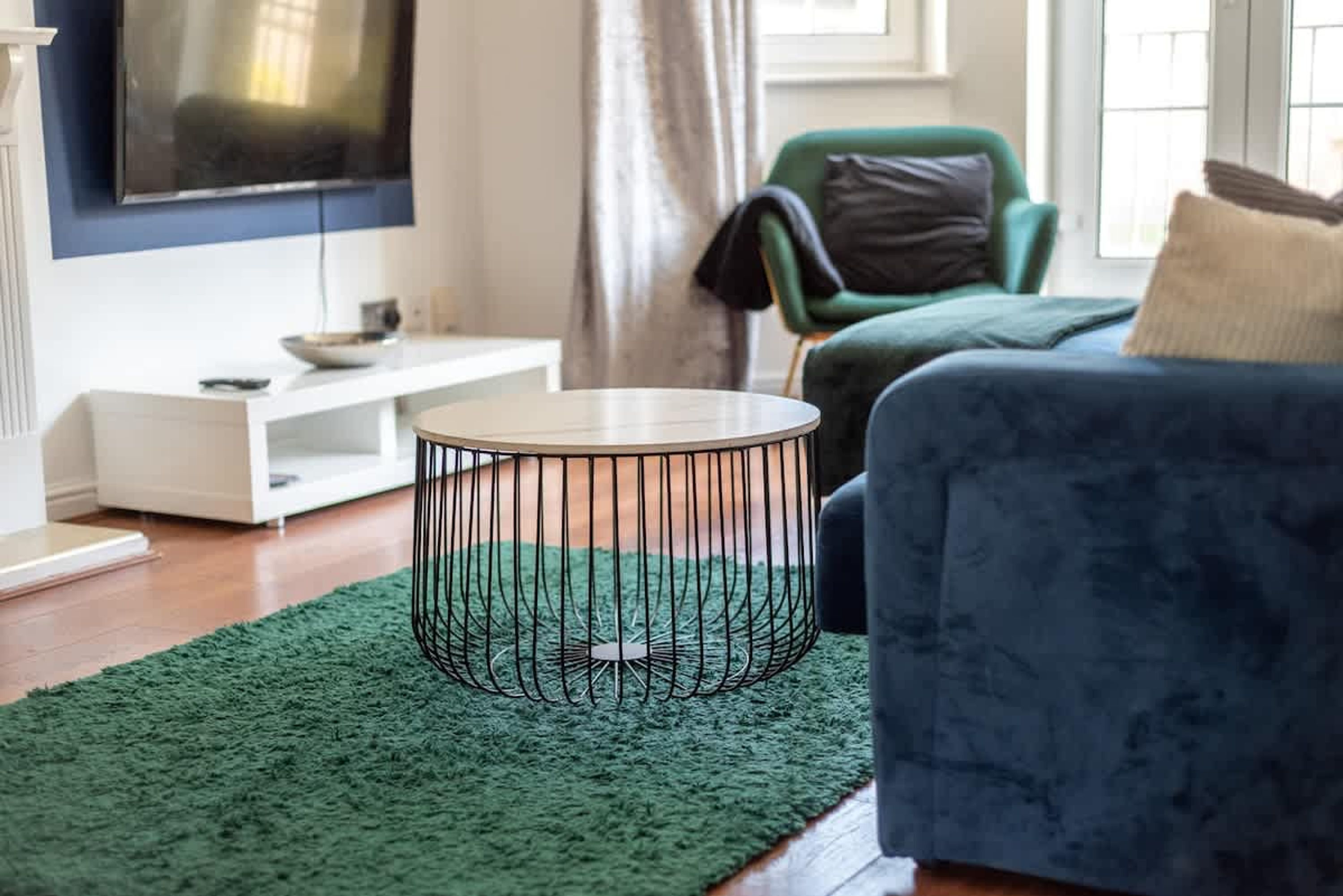 Ett modernt vardagsrum med ett runt soffbord, en blå soffa och en platt-TV som är monterad på väggen.
