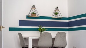 Ein Essbereich mit einem weißen Tisch, grauen Stühlen und türkis-blauen Zierstreifen an der Wand.