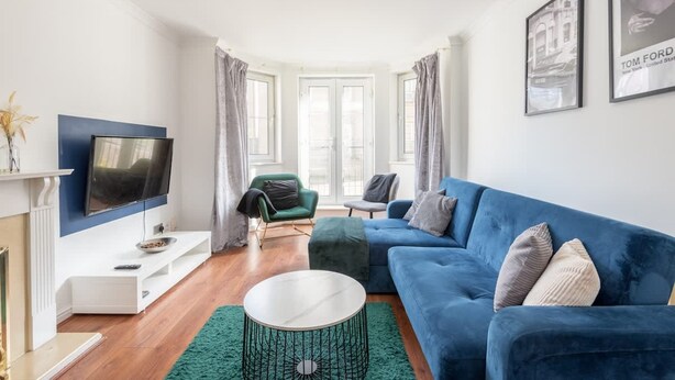 Ein modernes Wohnzimmer mit einem blauen Sofa, einem Flachbildfernseher und einem grünen Teppich.