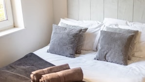 Ein ordentlich bezogenes Bett mit gestreiften Kissen und einer braunen Decke, ein Fenster mit Tageslicht und ein hölzernes Kopfteil.