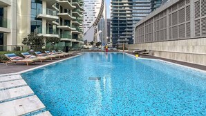 Una piscina con sillones de descanso y vistas a altos edificios.