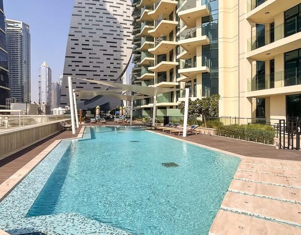Piscina no terraço com espreguiçadeiras e vista para edifícios altos ao redor.