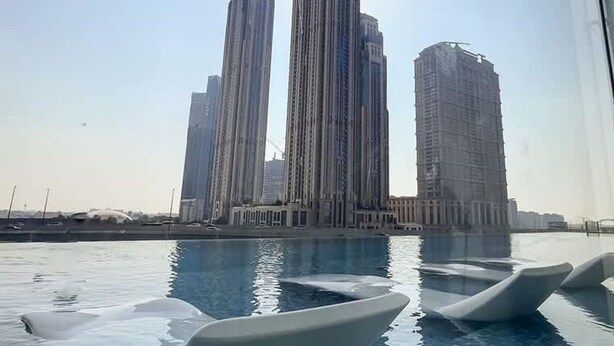 A pool with modern, white, boat-shaped loungers and a view of tall, modern buildings in the background. - Stylish Missoni-branded Studio (Dubai)