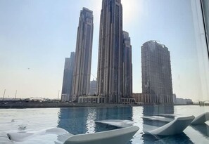 Piscina com espreguiçadeiras brancas e modernas em formato de barco, com vista para edifícios altos e contemporâneos ao fundo.
