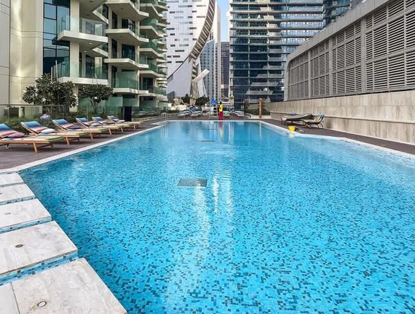 Une piscine avec des chaises longues et une vue sur les immeubles de grande hauteur.