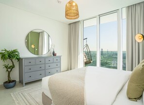 Ein Schlafzimmer mit einem Bett, einem Schminktisch, einem runden Spiegel, einem Hängekorbsessel und einem großen Fenster mit Blick auf die Stadt.