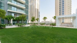 A modern building with multiple high-rise structures, a well-maintained grassy area, and a covered seating area. - Homesgetaway-luxury 2Br Apartment in Beach Vista Tower 2 With Beach Access (Dubai)