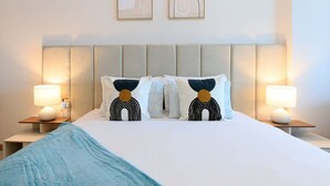 A hotel room with a bed, two nightstands, two wall-mounted lamps, and two framed pictures above the bed. - Business Bay - 1BR Missoni Branded Apartment (Dubai)
