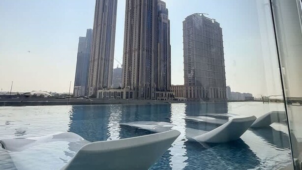 A swimming pool with modern, white loungers and a view of tall, modern buildings in the background. - Business Bay - 1BR Missoni Branded Apartment (Dubai)