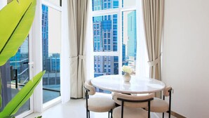 A modern room with a round table, two chairs, a vase with flowers, and a large window with curtains. - Business Bay - 1BR Missoni Branded Apartment (Dubai)