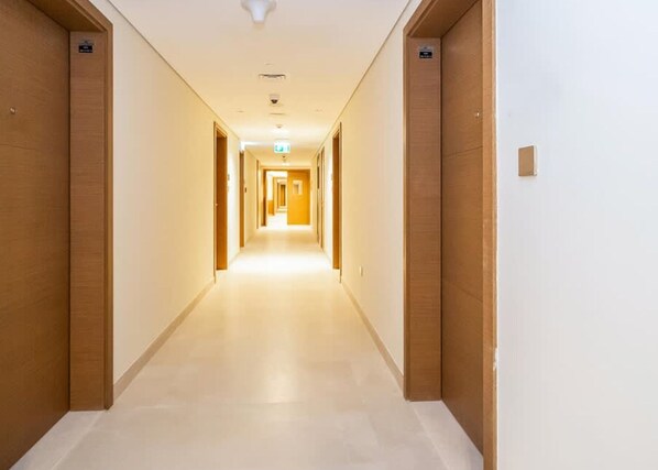 A hotel hallway with wooden doors, a tiled floor, and a ceiling light fixture. - Missoni-branded Residence Along Business Bay Canal (Dubai)