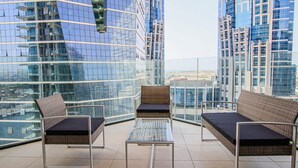 Ein hoher Balkon mit modernen Korbmöbeln, Glasgeländern und Blick auf die Stadt.