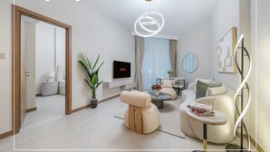 A modern living room with a sofa, a coffee table, a TV, and a potted plant. - 1BR on Dubai Canal 5 Mins to Burj Dubai Mall (Dubai)