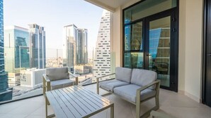 A balcony with a sofa and a table, overlooking a cityscape with modern buildings. - 1BR on Dubai Canal 5 Mins to Burj Dubai Mall (Dubai)