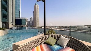 A rooftop pool area with a view of a city skyline, including a tall building. - 1BR on Dubai Canal 5 Mins to Burj Dubai Mall (Dubai)