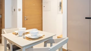 A dining area with a white table set for two, a wooden door, and a white wall with a small picture frame. - Sophisticated Studio Escape Missoni Luxury Design (Dubai)