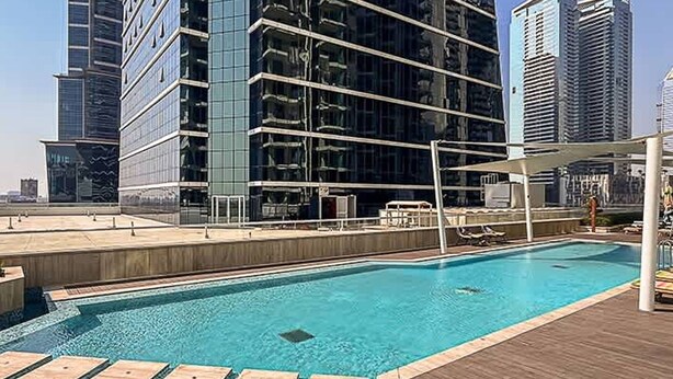 A rooftop pool with a wooden deck, surrounded by high-rise buildings. - Sophisticated Studio Escape Missoni Luxury Design (Dubai)