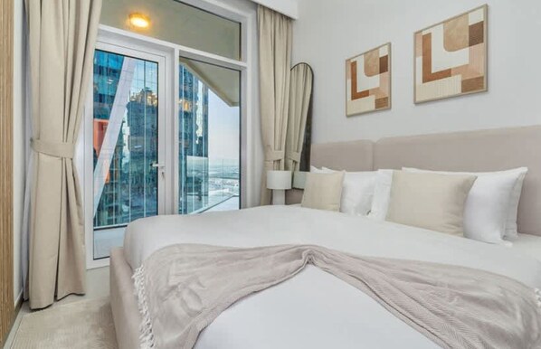 A hotel room with a large bed, a view of a cityscape through floor-to-ceiling windows, and abstract wall art. - 2BR Missoni Apt 5 min Drive to Burj Dubai Mall (Dubai)