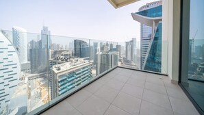 Un balcon moderne offrant une vue sur la ville, doté de garde-corps en verre et d’un sol carrelé.