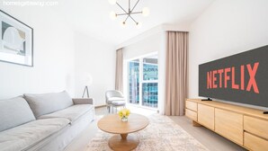 Un salon moderne avec un canapé gris, une table basse ronde ornée de fleurs, un meuble TV en bois et un grand téléviseur affichant le logo de Netflix.