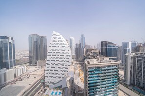 A modern cityscape with high-rise buildings, including a distinctive curved structure and a building under construction. - Stunning 2BR Missoni High-floor Breathtaking Views (Dubai)
