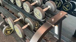 Un gimnasio con estanterías llenas de mancuernas, un espejo y equipo de ejercicio al fondo.
