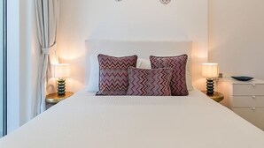 Una cama bien hecha con almohadas estampadas, dos lámparas de noche y un pequeño adorno en la pared.