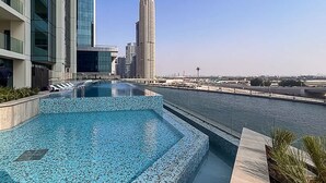 A rooftop pool with a view of modern buildings and a body of water. - Stylish 2BR Fully Furnished Unit at Missoni (Dubai)